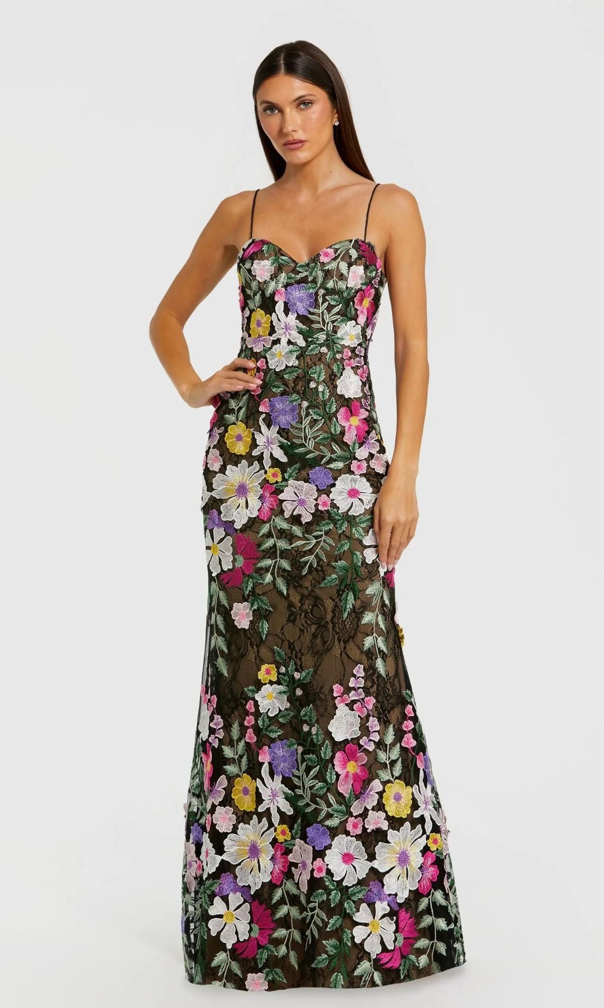 A woman models the Mac Duggal 68897 Long Formal Dress in Black Multi, a floor-length sleeveless gown with thin straps and a colorful floral pattern over sheer black fabric, against a plain white background.